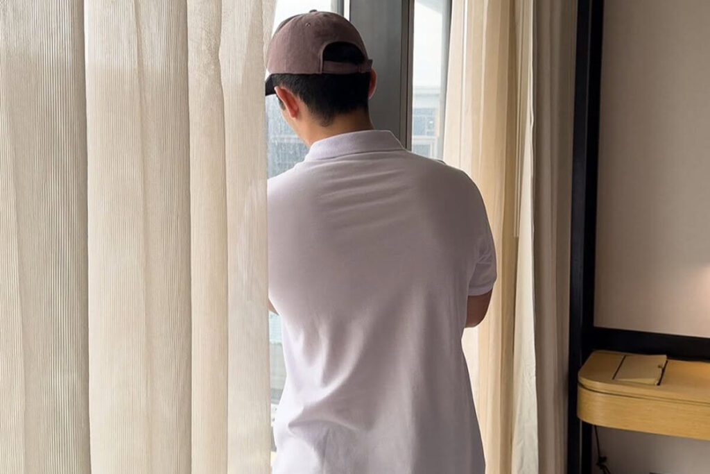 Man wearing a white plain shirt while standing near a window