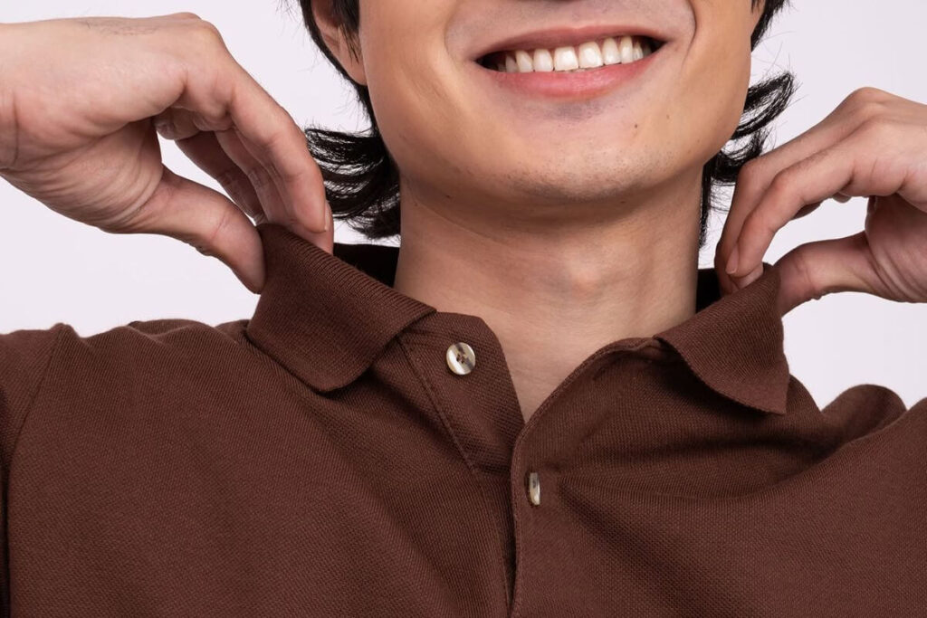 Male model adjusting the collar of a brown polo shirt