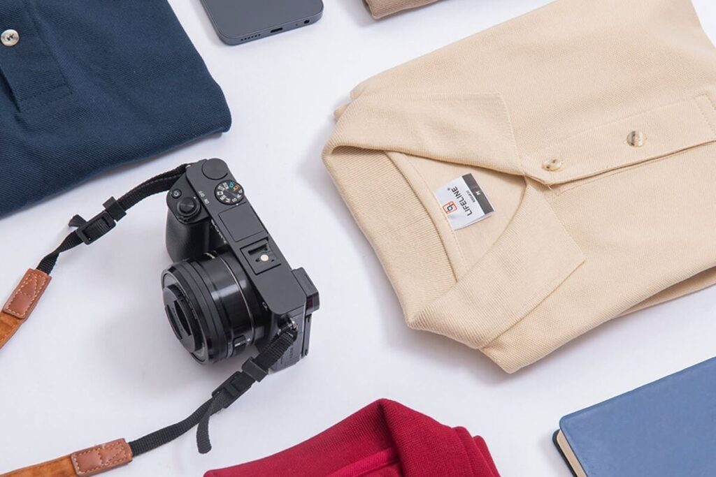 Folded Lifeline polo shirts with camera and notebook on a product styling table